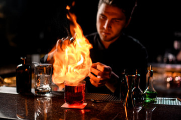 Bartender serving the red alcoholic cocktail with ice cubes under the fire