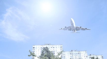 Bottom view of the plane over the house in the city. The sun shines.