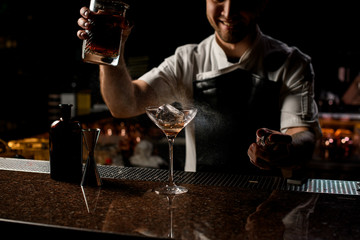 Professional bartender spraying on the brown alcoholic drink with a bitter to serve it