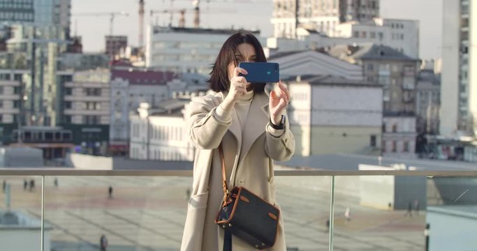 Confident Caucasian woman taking photos on city street. Businesslady standing at the background of skyscrapers and using smartphone. Lifestyle, hobby. Cinema 4k ProRes HQ.
