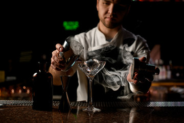 Professional male bartender holding in hands a steel shaker open it with the steam