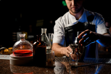 Professional male bartender holding in hands a steel shaker open it near the bartender equipment