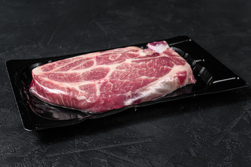 Unopened vacuum pack of pork steak isolated on black background, without label. Black background. Top view. Space for text