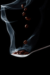 Spoon with hot coffee beans with smoke on a black background with falling coffee beans
