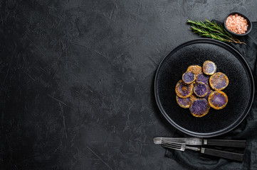 Baked purple potatoes with rosemary. Black background. Top view. Space for text