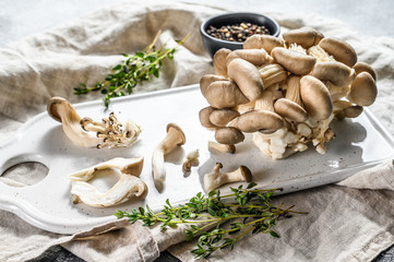 Fresh oyster mushrooms on a white chopping Board with thyme. Gray background. Top view