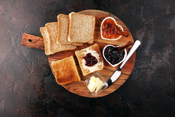Toast bread with homemade strawberry jam and apricot marmalade on rustic table served with butter...