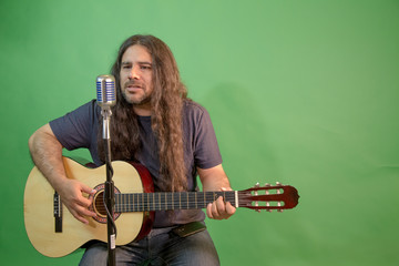 Singer with beard, hat and long hair in front of retro microphone, playing acoustic guitar, hipster...