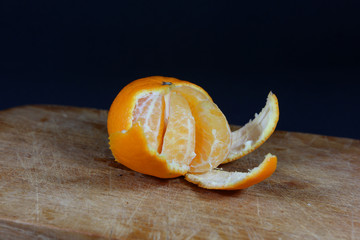 Partially peeled tangerine coming off two pieces on a wooden board with black background