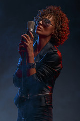 Young attractive sexy girl with curly hair in the form of a rock singer in a leather jacket