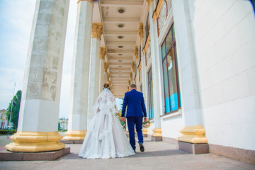 Newlyweds are walking among the columns, the bride is holding a wedding bouquet in her hands, they are standing with  © popovatetiana