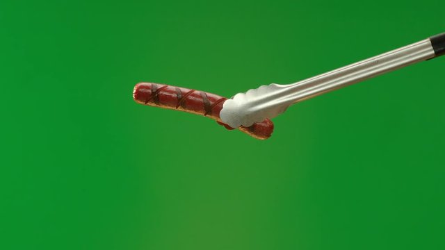 Hot dog grilled on green screen moved around by tongs