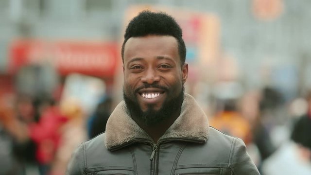 Close-up young adult American black man in jacket smiling and looking at camera. Smile human. Cold winter in New York. Happy african people in city on street closeup look. Male laughing. White teeth.