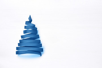 Christmas tree made from blue ribbon on white background. Copy space, top view. Color of the year...