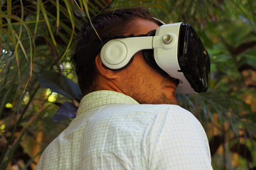 Portrait of a Man in VR 360, virtual reality 3D headset and exploring the play on a background of tropical jungle.