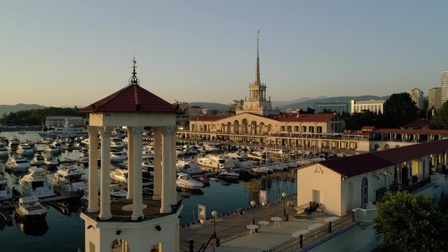 Aerial approach marine station Sochi Russia best sight beautiful cityscape reflection in water. Orange sunset port many modern yacht boats. People tourists walk pedestrian embankment resort town life