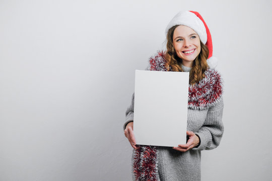 Beautiful girl wearing Santa hat with white empty canvas board for Christmas message. Mockup poster. 