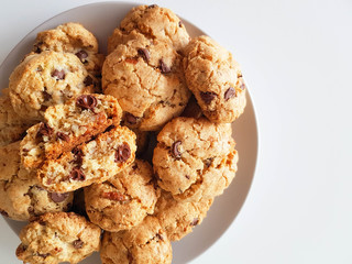 Homemade oatmeal cookies with pecan nuts and milk chocolate on a light grey plate on a white background