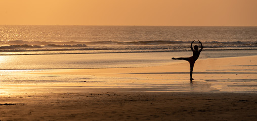 silhouette of a girl doing yoga in the beach in bali , at sunset 