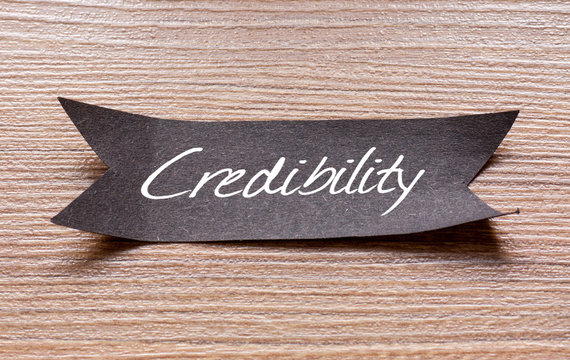 Credibility word written on Black papper with wooden background