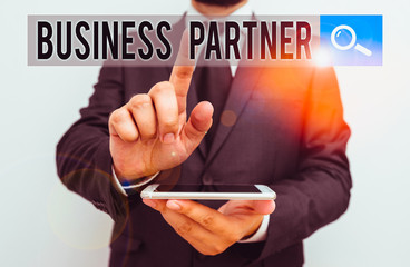 Writing note showing Business Partner. Business concept for commercial entity with which another commercial entity Male human wear formal work suit hold smartphone using hand