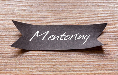 Mentoring word written on Black papper with wooden background