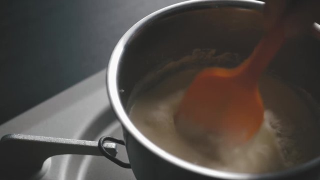Mixing flour and milk with a polyester spoonin a sause pan on gaz range. close up shot.