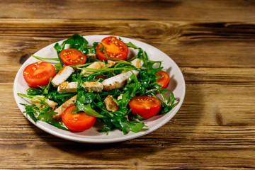 Tasty salad of fried chicken breast, fresh arugula and cherry tomatoes on wooden table