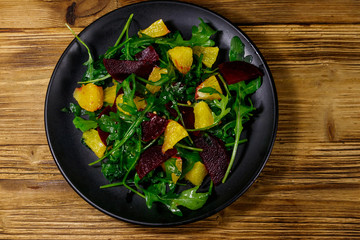 Tasty salad of fresh arugula, beetroot and oranges on wooden table. Top view. Healthy food or vegetarian concept