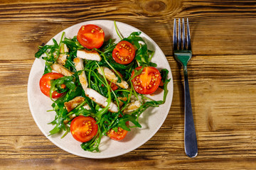 Tasty salad of fried chicken breast, fresh arugula and cherry tomatoes on wooden table. Top view