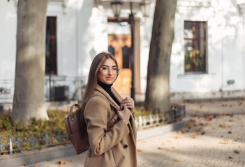 A young woman dressed in a coat and with a backpack is walking in the autumn European city