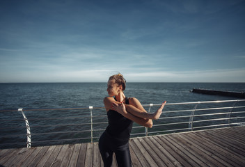 Fototapeta premium Slim fit woman in sportswear doing stretching hand exercise on the beach at bright sunny day
