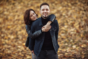 Fototapeta premium Portrait of a young hugging couple of lovers on a blurry background of fallen autumn leaves in the park.