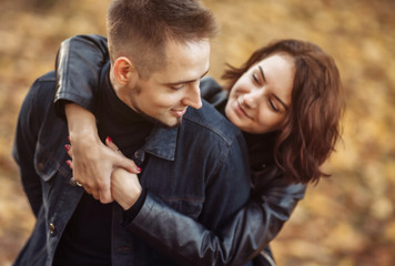 Portrait of a young hugging couple of lovers on a blurry background of fallen autumn leaves in the park.