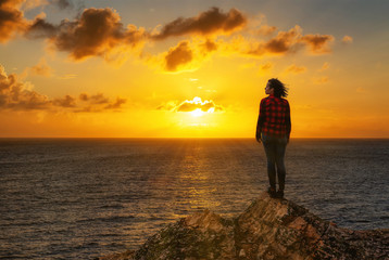 Adventurous Girl on a Rocky Ocean Coast enjoying the beautiful view of the Colorful Sunset. Image Composit. Adventure, Travel, Explore Concept.