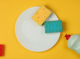 Washing dishes. Plate with sponges, a bottle of washing gel on yellow background. Top view. Studio shot.