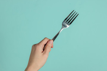 Female hand holds a fork on blue pastel background. Top view. Studio shot