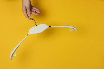 Female hand holds clothes hanger on yellow background. Minimalistic fashion concept. Studio shot....