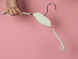 Female hand holds clothes hanger on pink pastel background. Minimalistic fashion concept. Studio shot. Top view