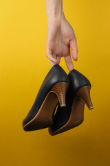 Studio fashion shot. Female hands holding classic high heel shoes on a yellow background