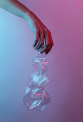 Recycling concept. Female hand holds a rumpled plastic bottle. Creative pop art pink blue neon color. Trendy gradient illumination. Night light