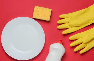 Set of tools for washing dishes on red studio background. Plate, rubber gloves, sponge, bottle. Top view. Flat lay