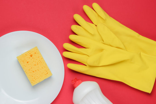 Set Of Tools For Washing Dishes On Red Studio Background. Plate, Rubber Gloves, Sponge, Bottle. Top View. Flat Lay