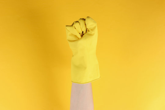 Femen symbol. Female fist in rubber gloves on a yellow studio background