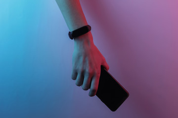 Female hand with smart bracelet and smartphone. Modern gadgets. Creative pop art pink blue neon color. Trendy gradient illumination