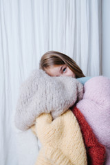 Little girl is hugging pile of soft fluffy multi-colored freshly washed sweaters, aside from the...