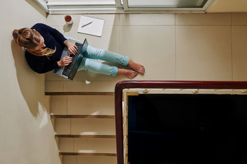 Young woman in casual clothes sitting on the floor and doing project for college on laptop