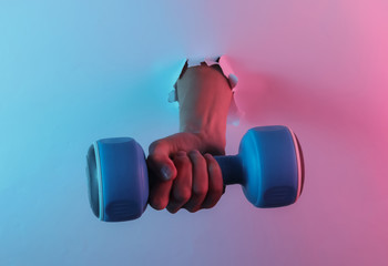 Hand holds dumbbell through torn hole. Creative pop art pink blue neon color. Trendy gradient illumination. Night light