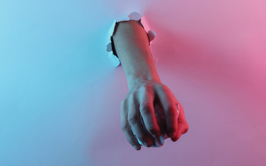 Hand holding crumpled paper ball through torn hole. Creative pop art pink blue neon color. Trendy gradient illumination. Night light