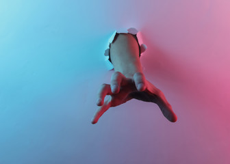 Mystical halloween concept. Hand through a torn hole. Creative pop art pink blue neon color. Trendy gradient illumination. Night light